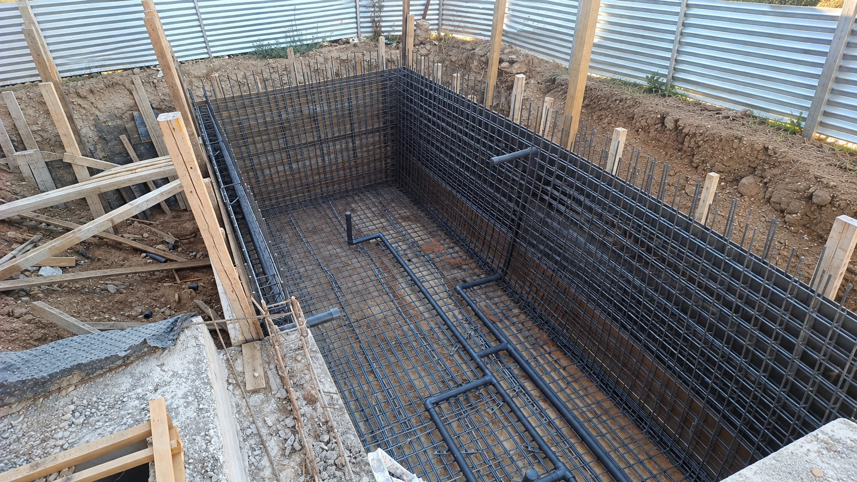 Reinforcement cages and buried pipework in a swimming pool shell before the concrete pour